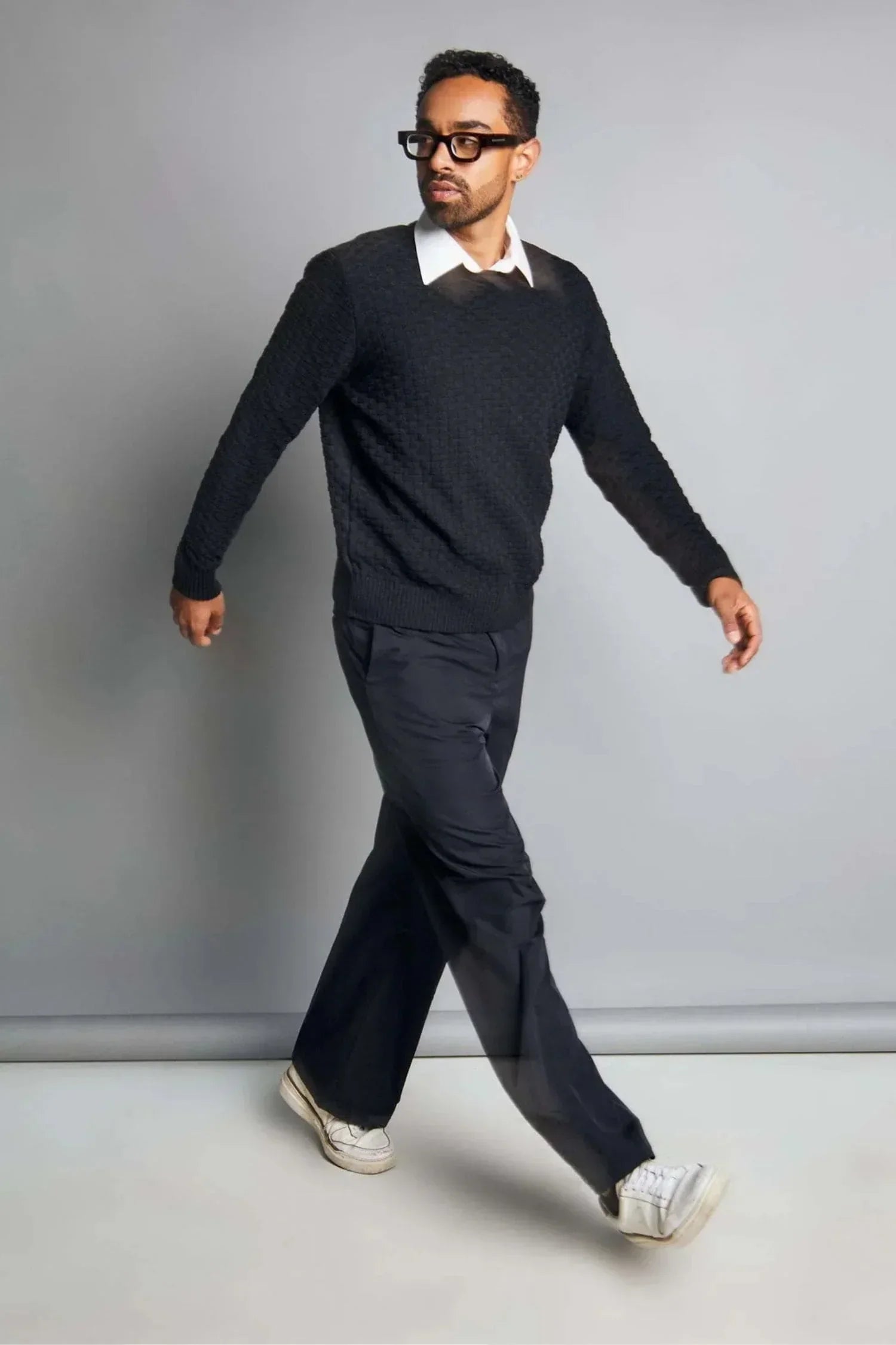 Hombre con suéter negro de punto, camisa blanca y pantalón oscuro, moda casual elegante